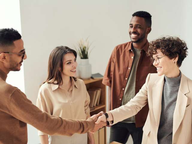 Four colleagues smiling and shaking hands in a bright office setting.